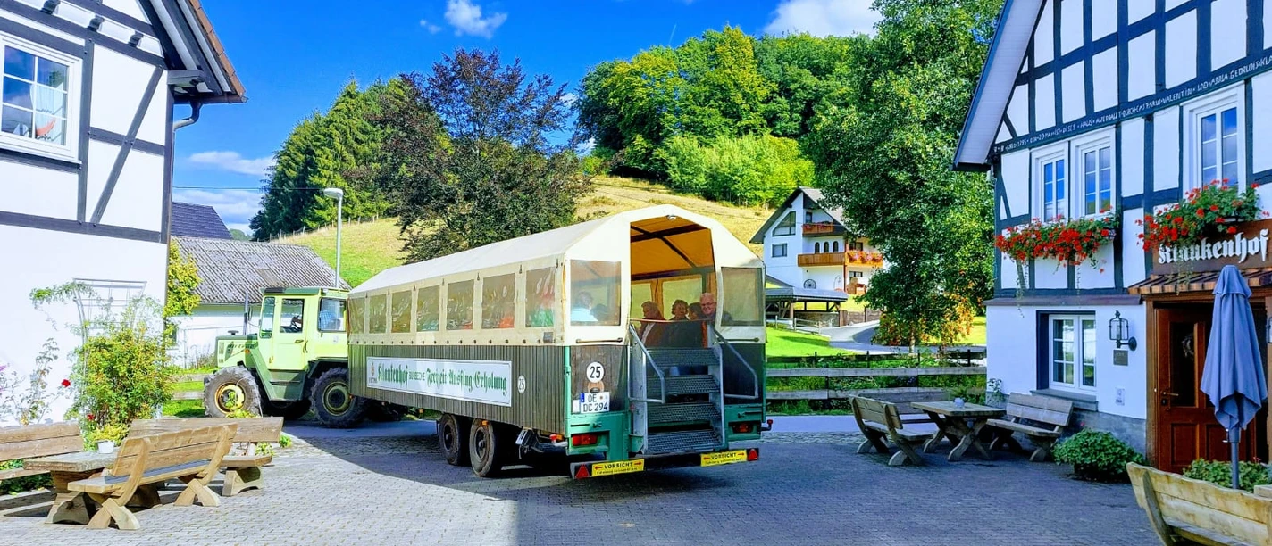 IMG-20220927-WA0002 (002).jpg Ein grüner Traktor zieht einen Planwagen zwischen zwei Fachwerkhäusern auf dem Klaukenhof.
