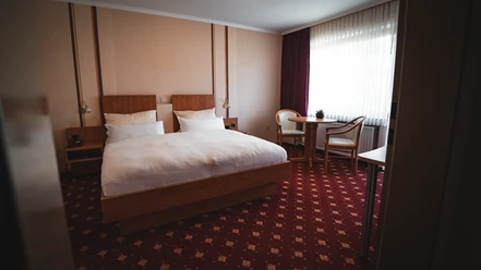 Doppelzimmer des Hotels Resi Doppelzimmer mit Holzbett, Sitzgruppe am Fenster und rotem Teppichboden.