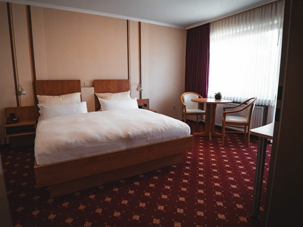 Doppelzimmer des Hotels Resi Doppelzimmer mit Holzbett, Sitzgruppe am Fenster und rotem Teppichboden.
