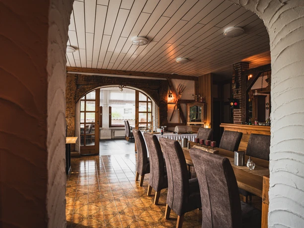 Gastraum des Hotels Resi Restaurantbereich mit langen Holztischen, gepolsterten Stühlen und Theke im Hintergrund.
