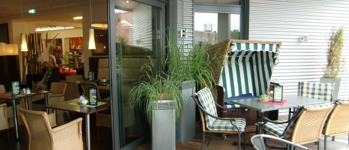 Café Textilwirtschaft der Rhauderfehner Erlebniswelt Terrasse des Cafés Textilwirtschaft mit Tischen, Stühlen und einem grün-weißen Strandkorb.