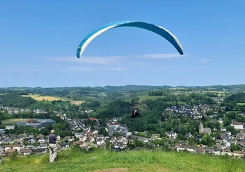 Gleitschirmflieger Hohe Hardt Gleitschirm über grüner Hügellandschaft mit Blick auf die darunterliegende Ortschaft