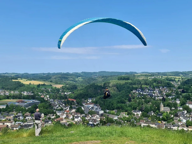 Gleitschirmflieger Hohe Hardt Gleitschirm über grüner Hügellandschaft mit Blick auf die darunterliegende Ortschaft