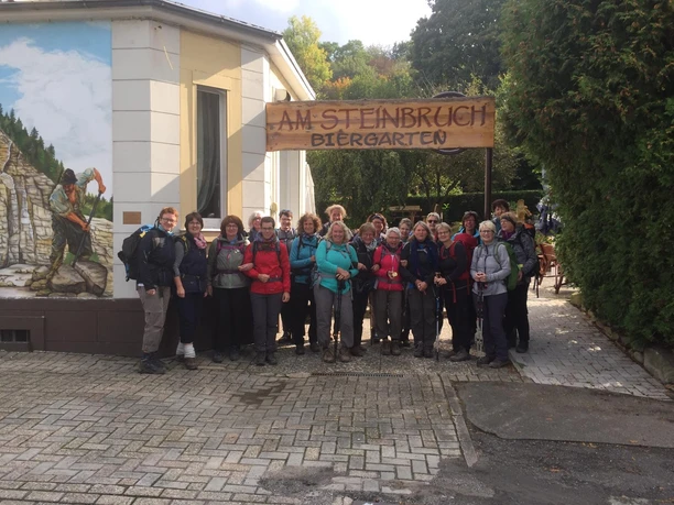 Eine Wandergruppe posiert fröhlich vor dem Restaurant & Café Am Steinbruch in Hilter im Freien.