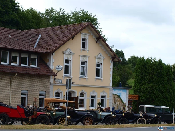 Historisches Gebäude im Grünen mit Oldtimern vor der Fassade, ideal für nostalgische Erlebnisse.