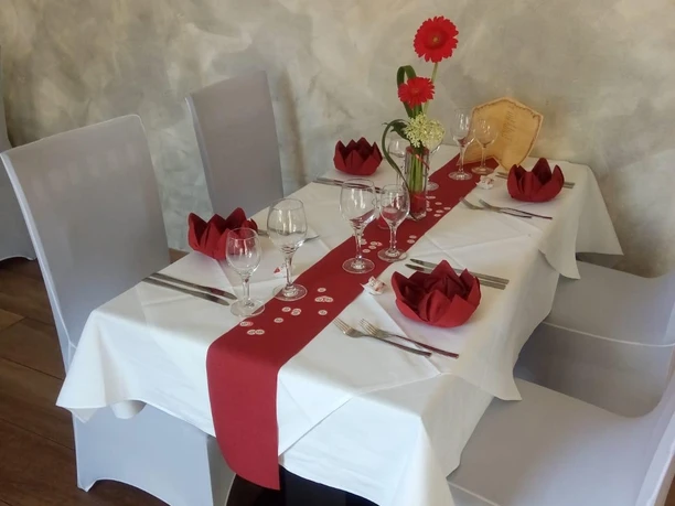 Gedeckter Tisch mit weißen Stuhlhussen und rotem Läufer, Blumenarrangement in Restaurantambiente.