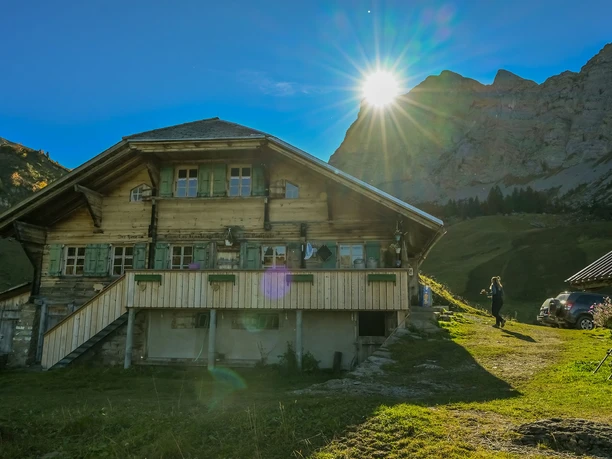 Berghaus Grimmi Ansicht der Alphütte, im Hintergrund kommt die Sonne hinter dem Berggipfel hervor