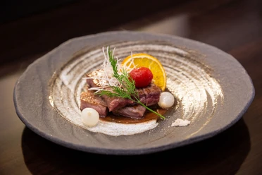 Restaurant Sakura Aachen Brand Tiefer Teller mit zwei Stücken Roast Beef, garniert mit Tomate, einer Orangenscheibe und Dill.