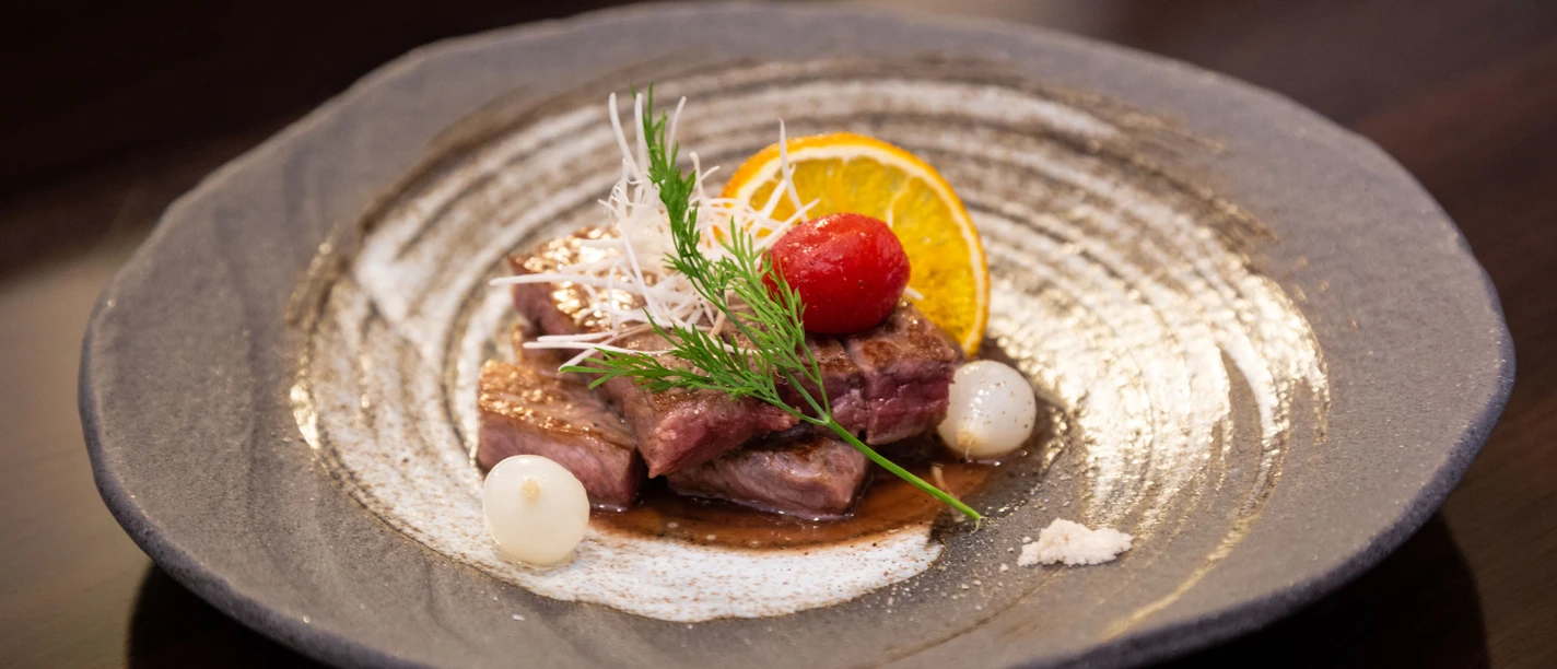 Restaurant Sakura Aachen Brand Tiefer Teller mit zwei Stücken Roast Beef, garniert mit Tomate, einer Orangenscheibe und Dill.