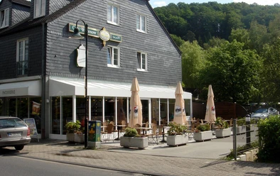 Café Rosenow Ein Café mit Außenterrasse, umgeben von Pflanzen, vor einem traditionellen Gebäude mit Schieferdach.