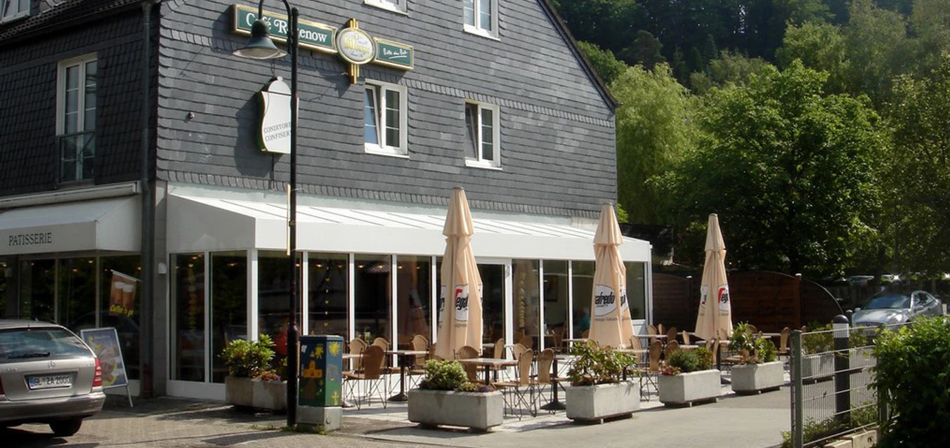 Café Rosenow Ein Café mit Außenterrasse, umgeben von Pflanzen, vor einem traditionellen Gebäude mit Schieferdach.