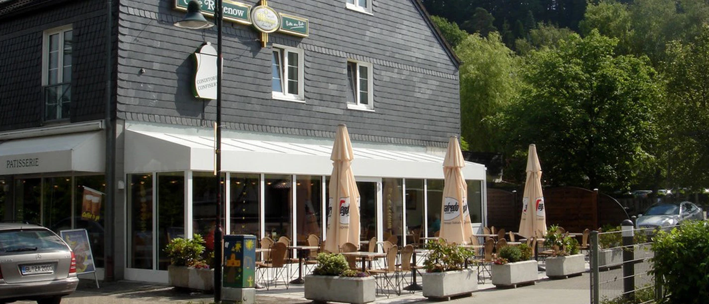 Café Rosenow Ein Café mit Außenterrasse, umgeben von Pflanzen, vor einem traditionellen Gebäude mit Schieferdach.
