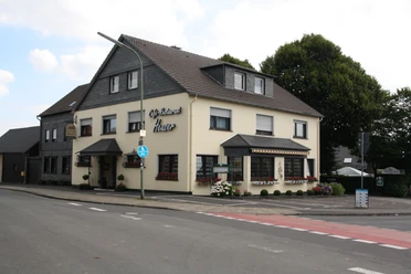 Café-Restaurant Heuser Ein traditionelles Gasthaus an der Straßenecke mit Schieferelementen und gepflegten Blumenbeeten.