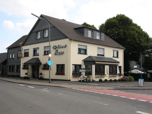 Café-Restaurant Heuser Ein traditionelles Gasthaus an der Straßenecke mit Schieferelementen und gepflegten Blumenbeeten.