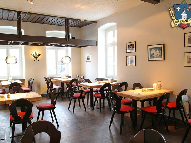 Gastraum Haus Kranenberg Gemütliches Restaurant mit Holztischen, roten Polsterstühlen und Wanddekorationen im traditionellen Stil.