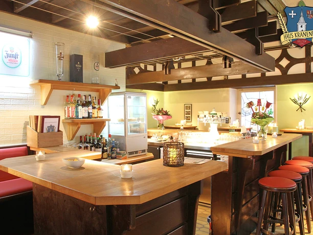 Gastraum Haus Kranenberg Gemütliche Bar mit Holztresen, Barhockern, beleuchteten Regalen und Dekorationen an den Wänden.