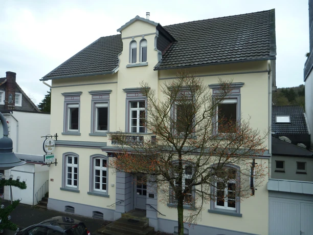 Haus Kranenberg Historisches, zweistöckiges Gebäude mit hellgelber Fassade und grauen Akzenten, vor kahlem Baum.