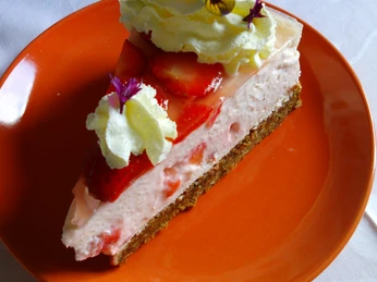 Kuchen Ein Stück Erdbeertorte mit Sahne und essbaren Blumen auf einem orangefarbenen Teller.
