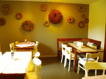 Innenbereich Gemütliches Café mit rustikaler Holzeinrichtung, weißen Stühlen und Dekor aus Trockenkränzen an der Wand.