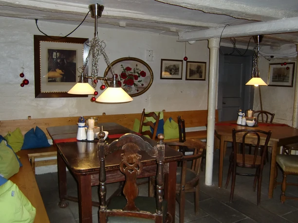 Die gute Stube Gemütliches Cafe mit rustikalen Holzmöbeln, Kissen und Wanddekorationen in warmem Licht.