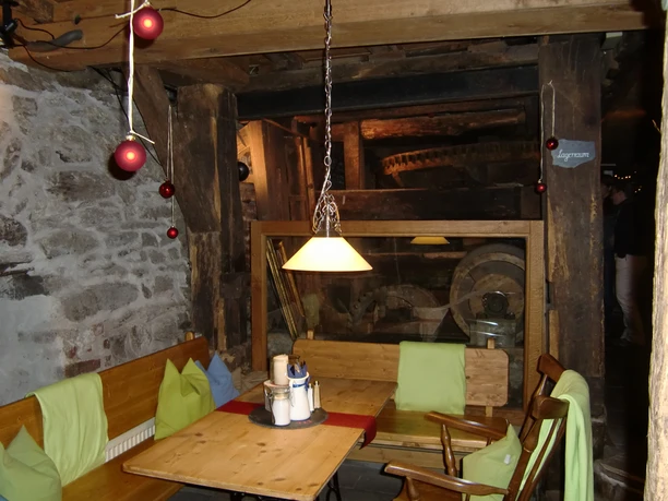 Innenbereich Gemütlicher Gastraum mit Holzmöbeln, Steinwänden und nostalgischer Mühlendekoration im Hintergrund.