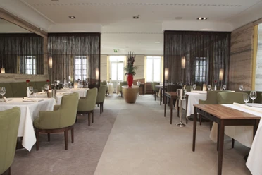 Innenansicht Restaurant Vendome Elegantes Restaurant mit gedeckten Tischen, grünen Stühlen und einer großen Blumenvase in der Mitte.