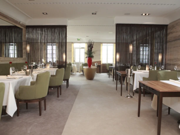 Innenansicht Restaurant Vendome Elegantes Restaurant mit gedeckten Tischen, grünen Stühlen und einer großen Blumenvase in der Mitte.