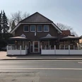 schlemmer-grill-haren Backsteinhaus mit zwei überdachten Terrassenbereichen und weißen Geländern an einer Straße.