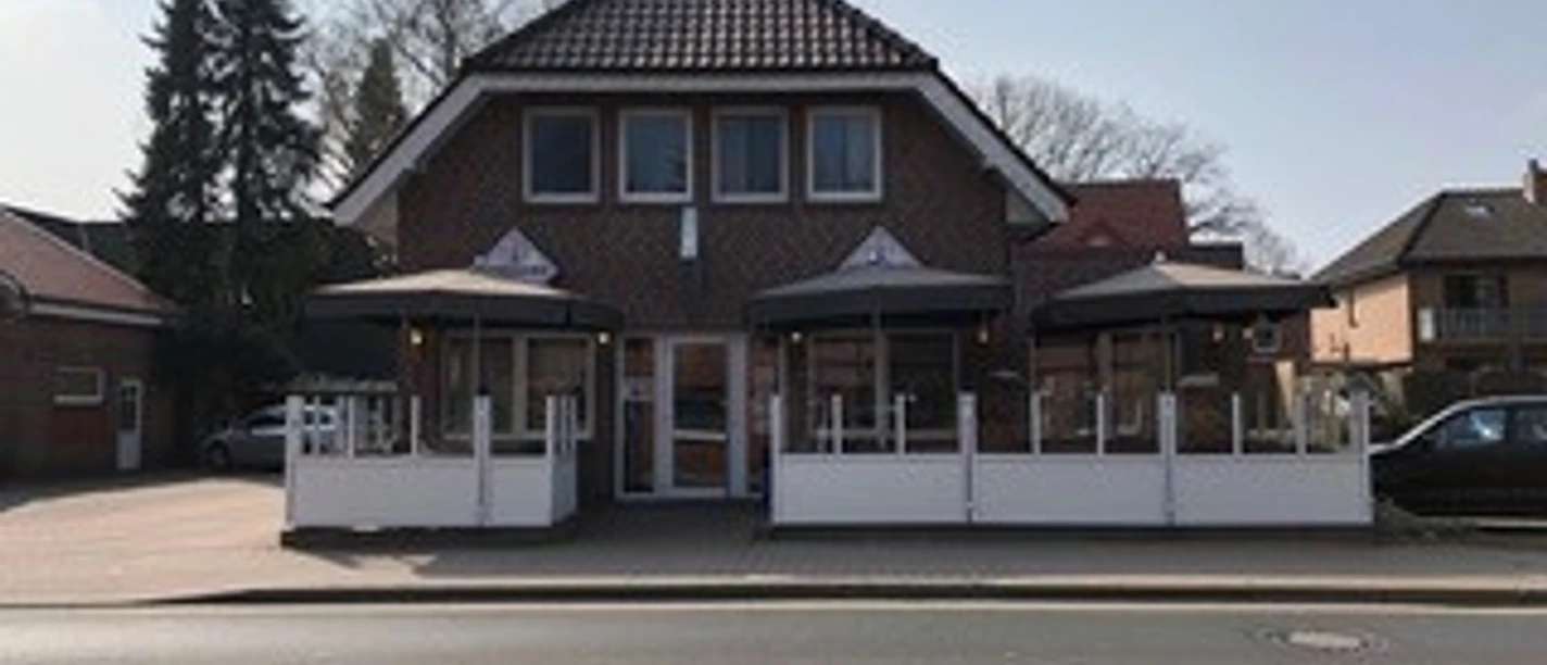 schlemmer-grill-haren Backsteinhaus mit zwei überdachten Terrassenbereichen und weißen Geländern an einer Straße.