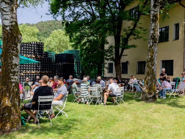Erzquell Brauerei Sommerfest Menschen sitzen auf Wiesenstühlen beim Brauereifest zwischen Bäumen und gestapelten Getränkekisten.