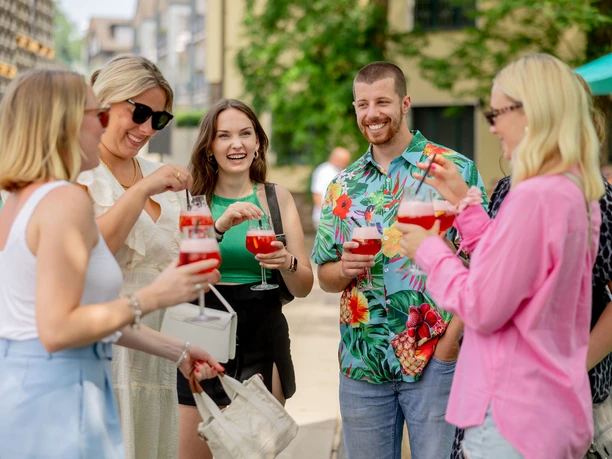 Erzquell Brauerei Sommerfest Gruppe junger Menschen feiert im Freien und hält farbige Getränke in der Hand