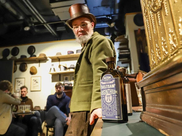 On the Trail of the Green Fairy - Absinthe tasting in Cologne Man with top hat next to absinthe bottle in historical room during tasting.