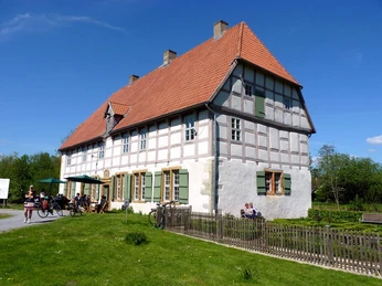 Werburg Fachwerkhaus mit rotem Ziegeldach und grünen Fensterläden, umgeben von Rasen und Besuchern im Freien.