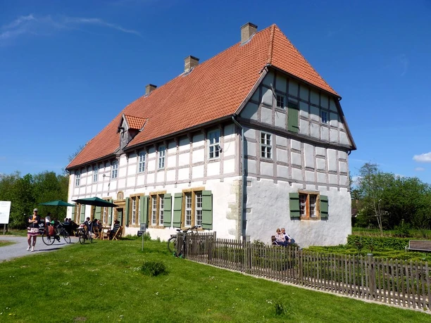 Werburg Fachwerkhaus mit rotem Ziegeldach und grünen Fensterläden, umgeben von Rasen und Besuchern im Freien.