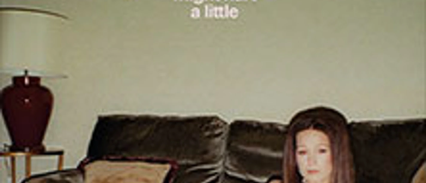Frau sitzt vor dunklem Sofa, daneben Lampe, darüber Albumtitel panicbaby *this might hurt a little