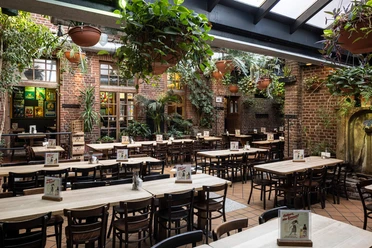 HELLERS Brauhaus Großer Innenhof mit Holztischen, Backsteinwänden und vielen hängenden Pflanzen.