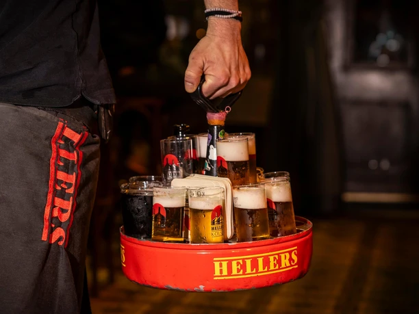 HELLERS Brewery A hand holds a red beer wreath with several filled glasses in a lively brewery atmosphere