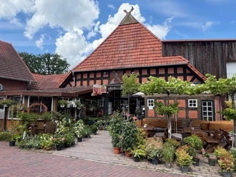 Das Fachwerkgebäude des Hofladens Holste, davor viele Pflanzen und Holzbänke zum Verweilen.