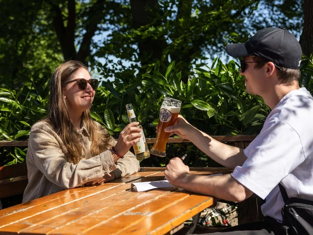 Schwimmbad Rhein-Sommergarten Two people are sitting at a wooden table in the outdoor area of a beer garden, enjoying their drinks.
