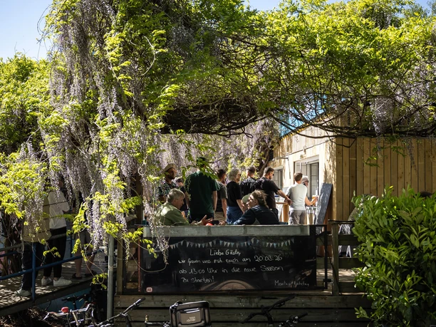 Schwimmbad Rhein-Sommergarten Personengruppe auf einer begrünten Terrasse, davor mehrere abgestellte Fahrräder bei sonnigem Wetter