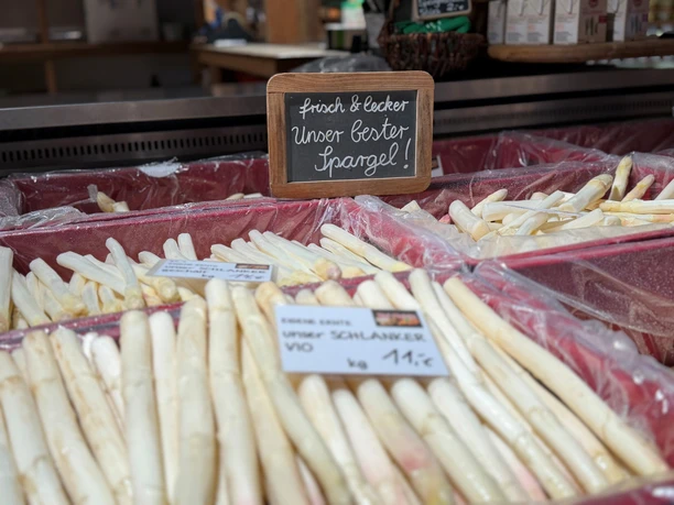 Fresh, white asparagus on display at a farm stand with a sign that reads "fresh & delicious."