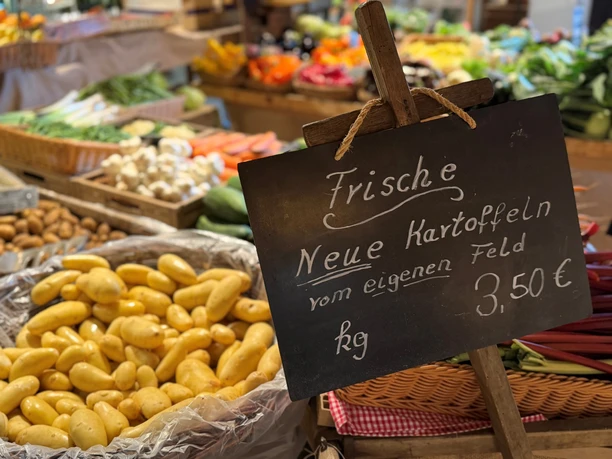 A handwritten sign for new potatoes from their own field, displayed in front of the produce display at the farm store.