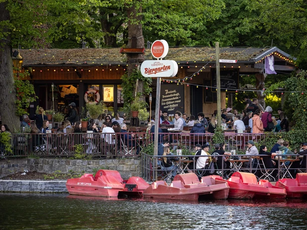 HELLERS Volksgarten A bustling beer garden by the water with red pedal boats and a dense canopy of green foliage