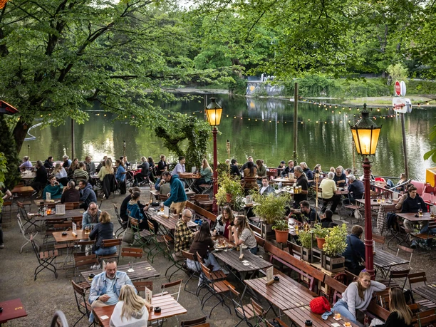 HELLERS Volksgarten A bustling beer garden under large trees by the lake in the evening light