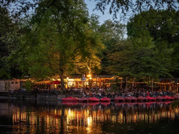 HELLERS Volksgarten Evening outdoor dining by the lake, with lights and red pedal boats under the trees