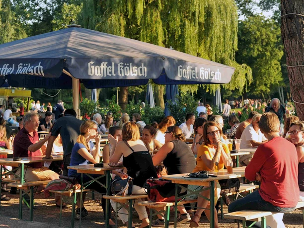 Beer Garden at Aachener Weiher People are sitting under large umbrellas in the beer garden, enjoying the sunny day