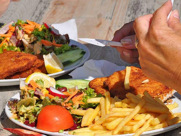Biergarten am Aachener Weiher Zwei Teller mit Schnitzel, Pommes und frischem Salat auf einem Holztisch im Freien