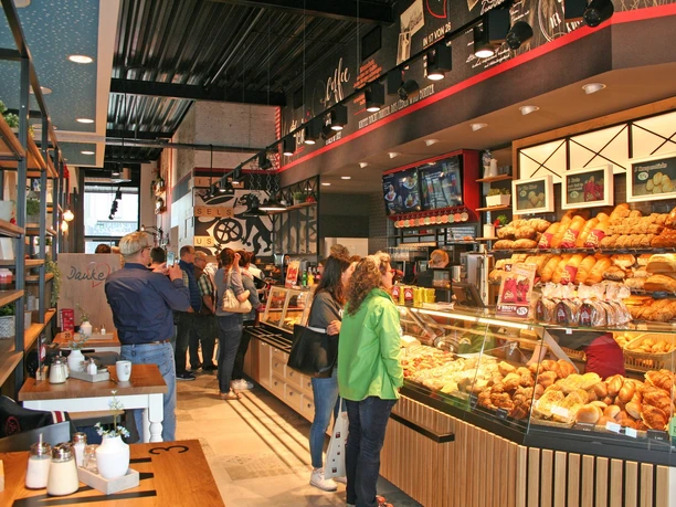 Bäckerei u. Konditorei Musswessels Rhauderfehn Innenansicht einer belebten Bäckerei mit Kunden an der Theke, die verschiedene Backwaren wie Brot und Croissants kaufen