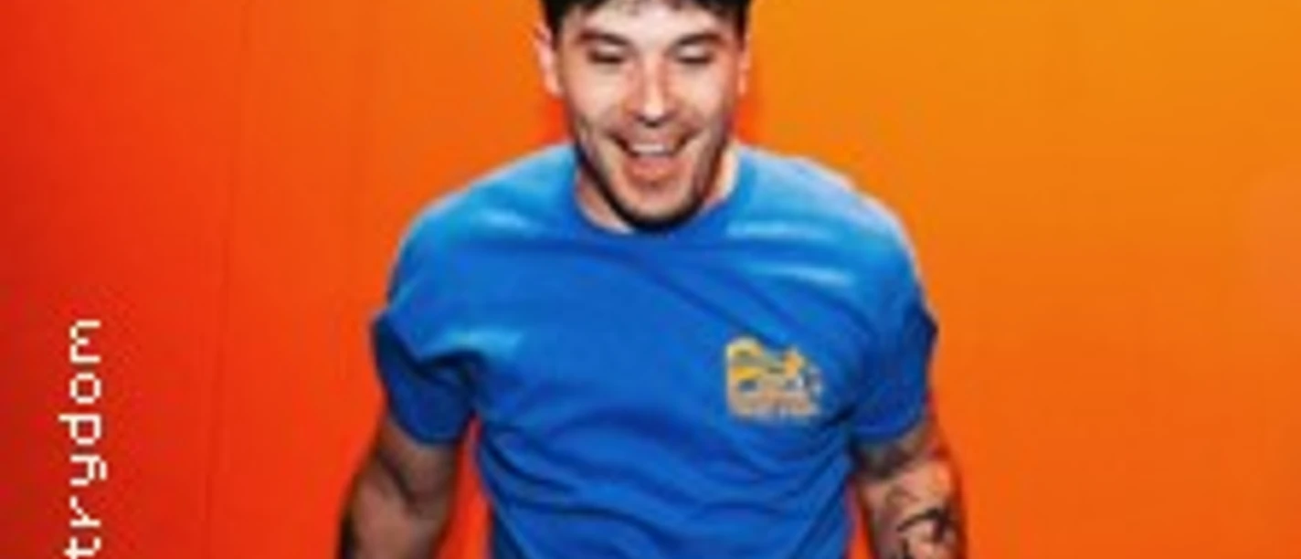 Matthew Mole springt vor orangefarbenem Hintergrund in blauem T-Shirt und Cap.