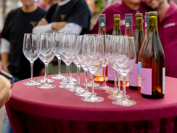 Waldbröler Weinfest Weingläser und Flaschen auf bordeauxrotem Stehtisch bei einem Fest mit Menschen im Hintergrund